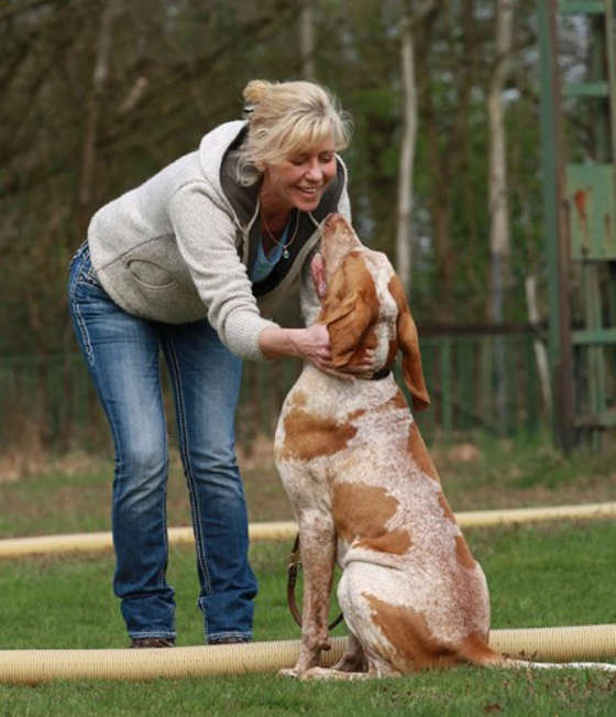 Susa Gülzow beugt sich auf dem Trainingsplatz zu einem orange-weißen Hund